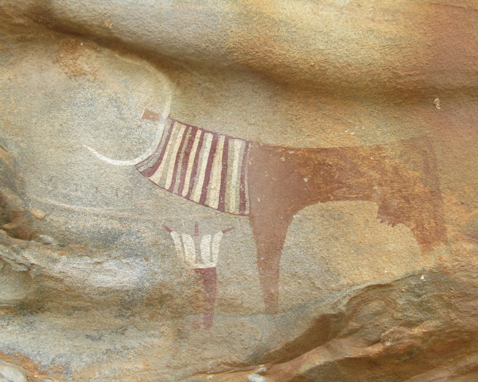 A Neolithic painting of a cow in a decorated collar, with a human figure beneath her, on the rock shelters at Laas Geel near Hargeisa
